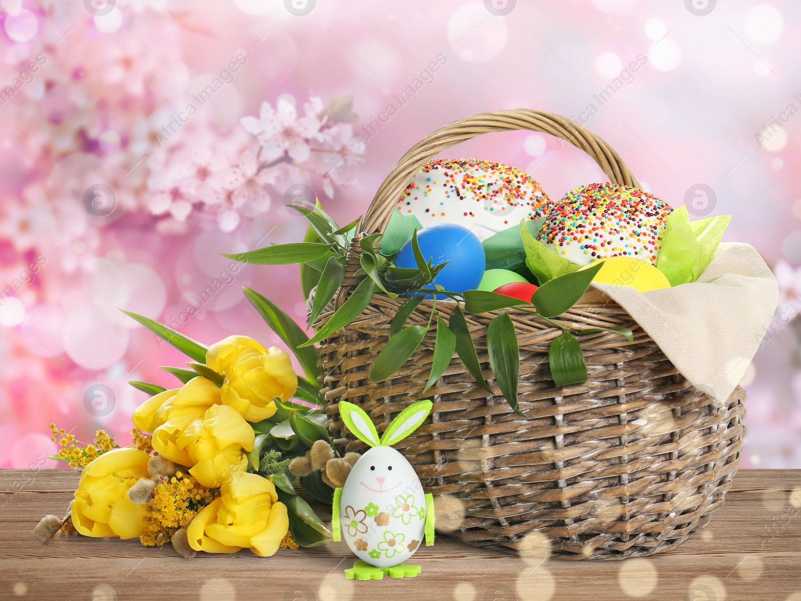 Image of Basket with delicious Easter cakes, dyed eggs and flowers on wooden table outdoors