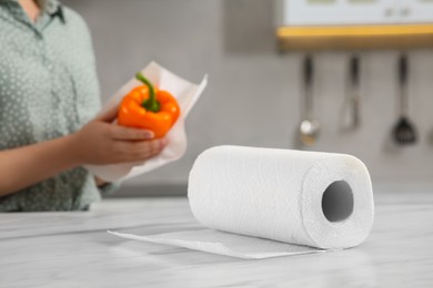Photo of Woman wiping bell pepper with paper towel at white marble table in kitchen, selective focus. Space for text