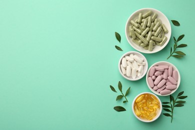 Photo of Different vitamin capsules in bowls and leaves on turquoise background, flat lay. Space for text