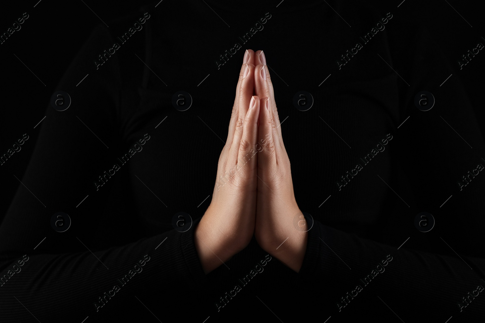 Photo of Woman holding hands clasped while praying in darkness, closeup