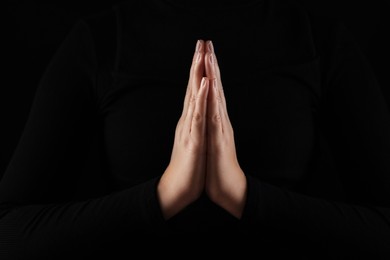 Photo of Woman holding hands clasped while praying in darkness, closeup