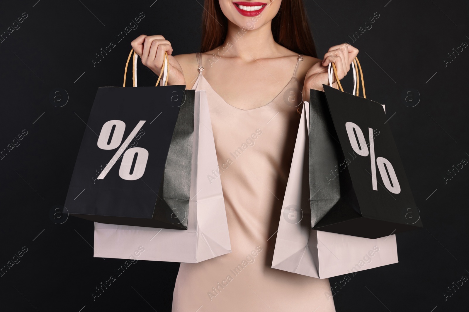 Image of Discount, sale, offer. Woman holding paper bags with percent signs against black background, closeup