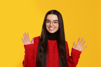 Portrait of happy teenage girl wearing glasses on yellow background