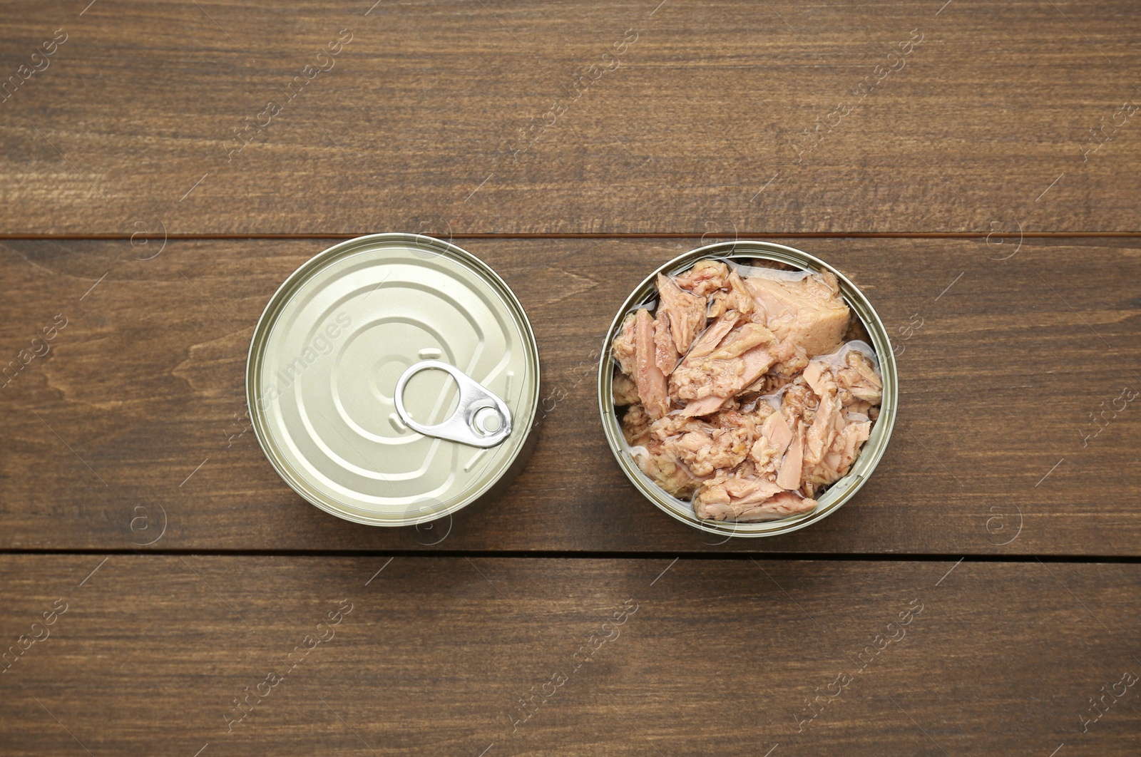 Photo of Tin cans with canned tuna on wooden table, flat lay