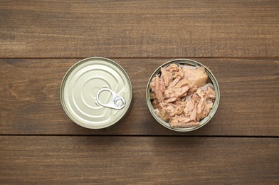 Tin cans with canned tuna on wooden table, flat lay