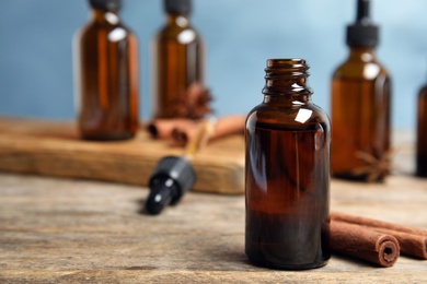 Photo of Bottle of essential oil and cinnamon sticks on wooden table against blue background. Space for text