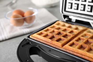 Photo of Modern iron with tasty Belgian waffles on grey table, closeup