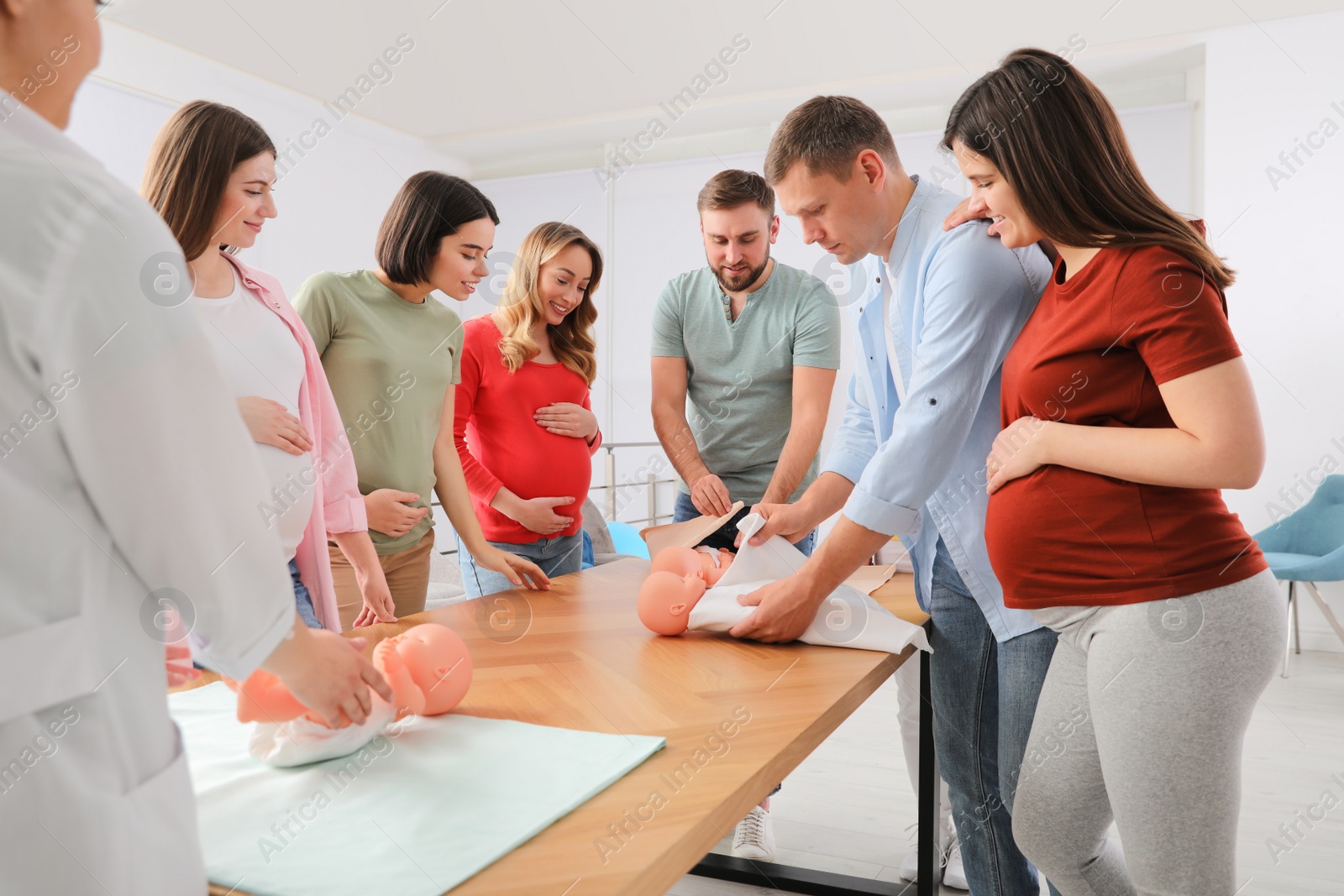 Photo of Future fathers and pregnant women learning how to swaddle baby at courses for expectant parents indoors