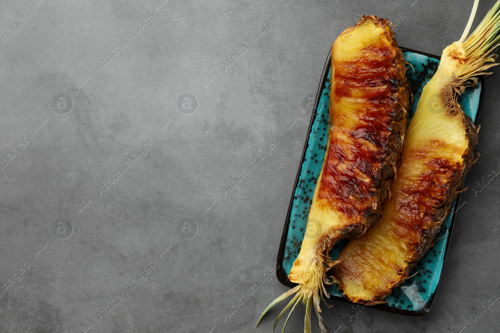 Photo of Tasty grilled pineapple pieces on grey textured table, top view. Space for text