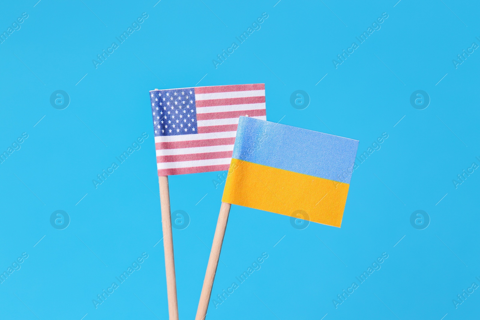 Photo of Small paper flags of Ukraine and USA on light blue background