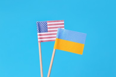 Photo of Small paper flags of Ukraine and USA on light blue background