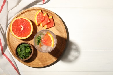 Photo of Delicious refreshing drink with sicilian orange and mint near fresh ingredients on white wooden table, flat lay. Space for text