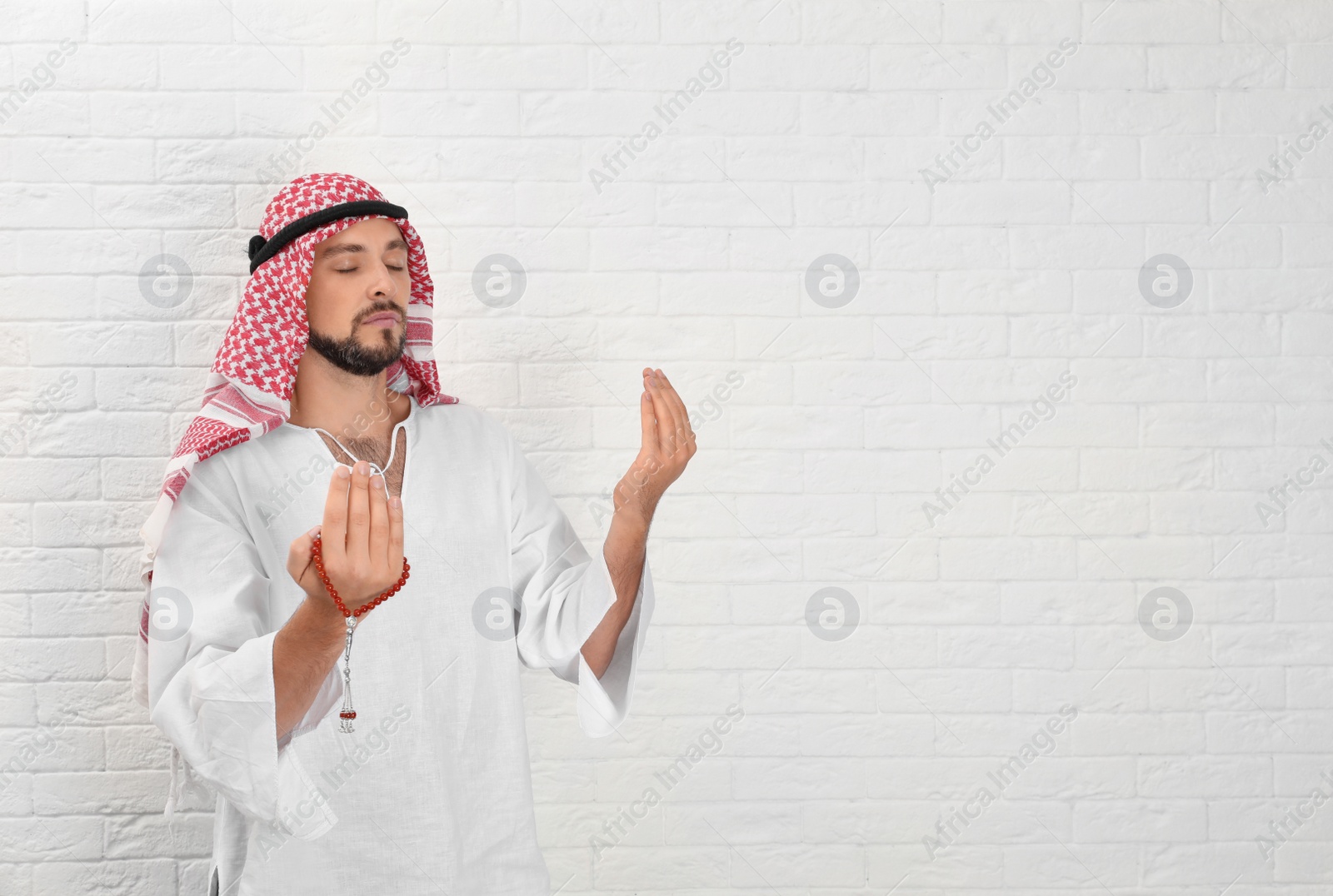 Photo of Muslim man praying near brick wall. Space for text