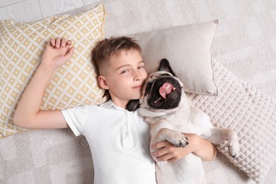 Photo of Boy with his cute pug lying on floor at home, top view