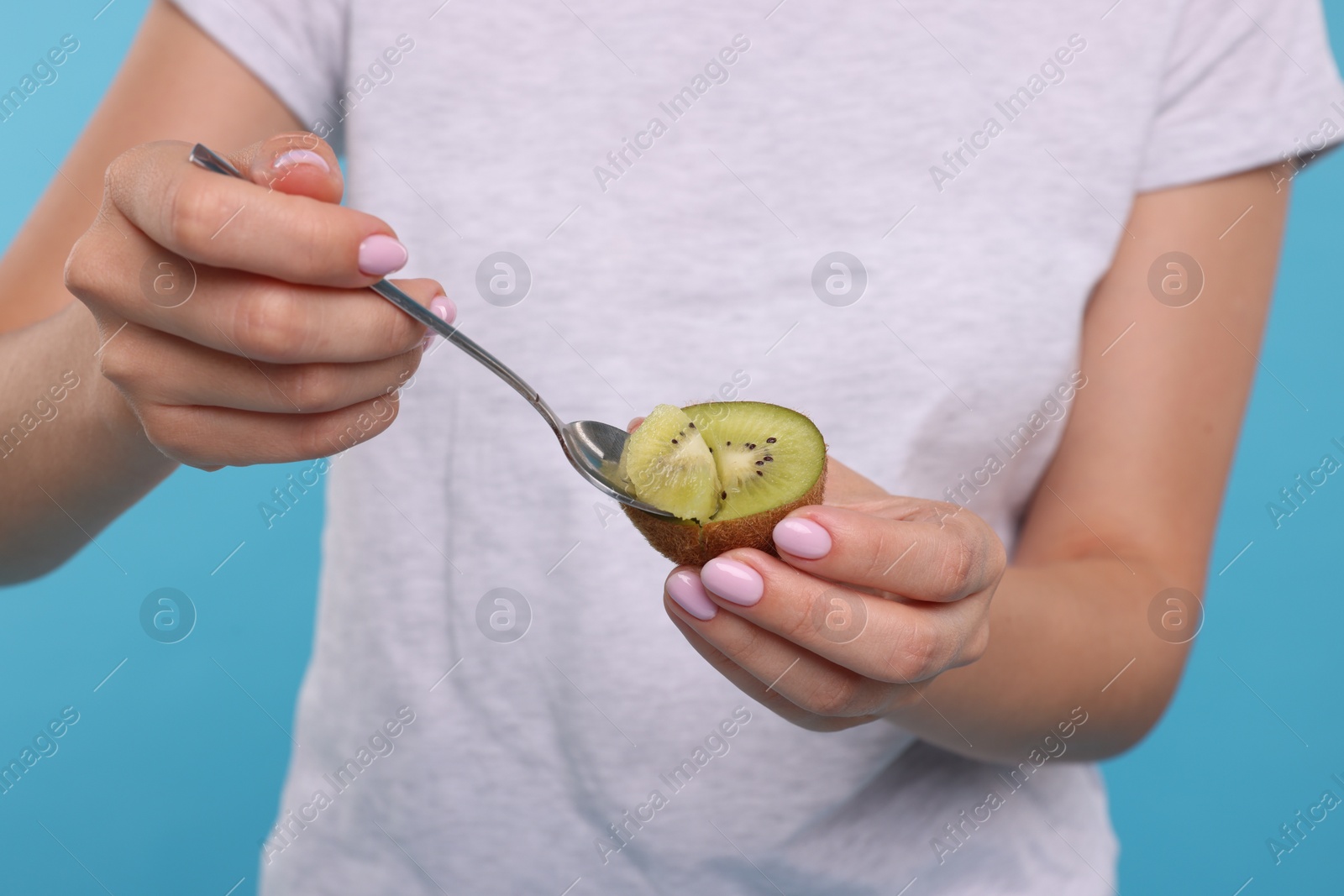 Photo of Woman eating kiwi with spoon on light blue background, closeup