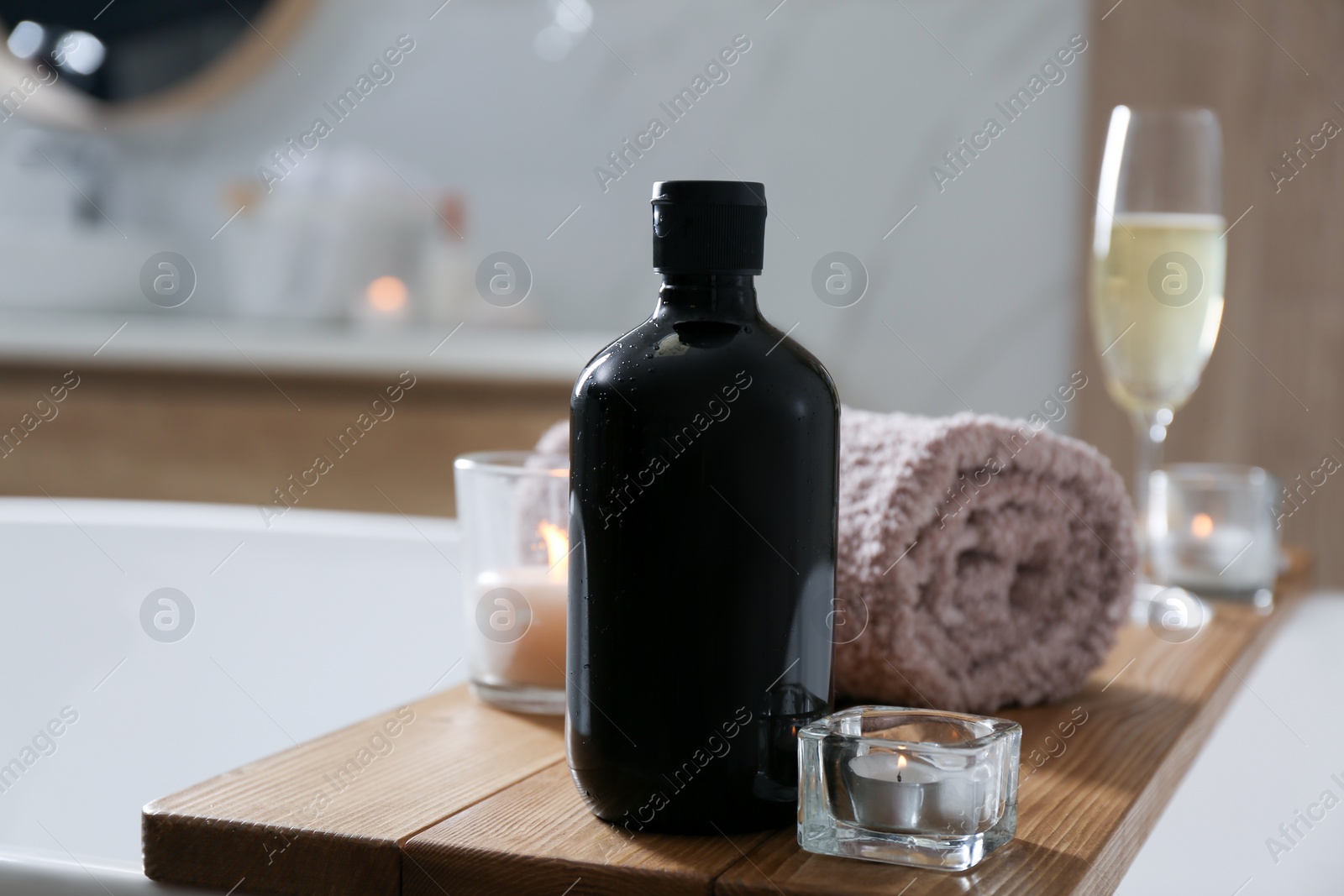 Photo of Wooden bath tray with shower gel, candles and fresh towel on tub indoors