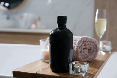 Wooden bath tray with shower gel, candles and fresh towel on tub indoors