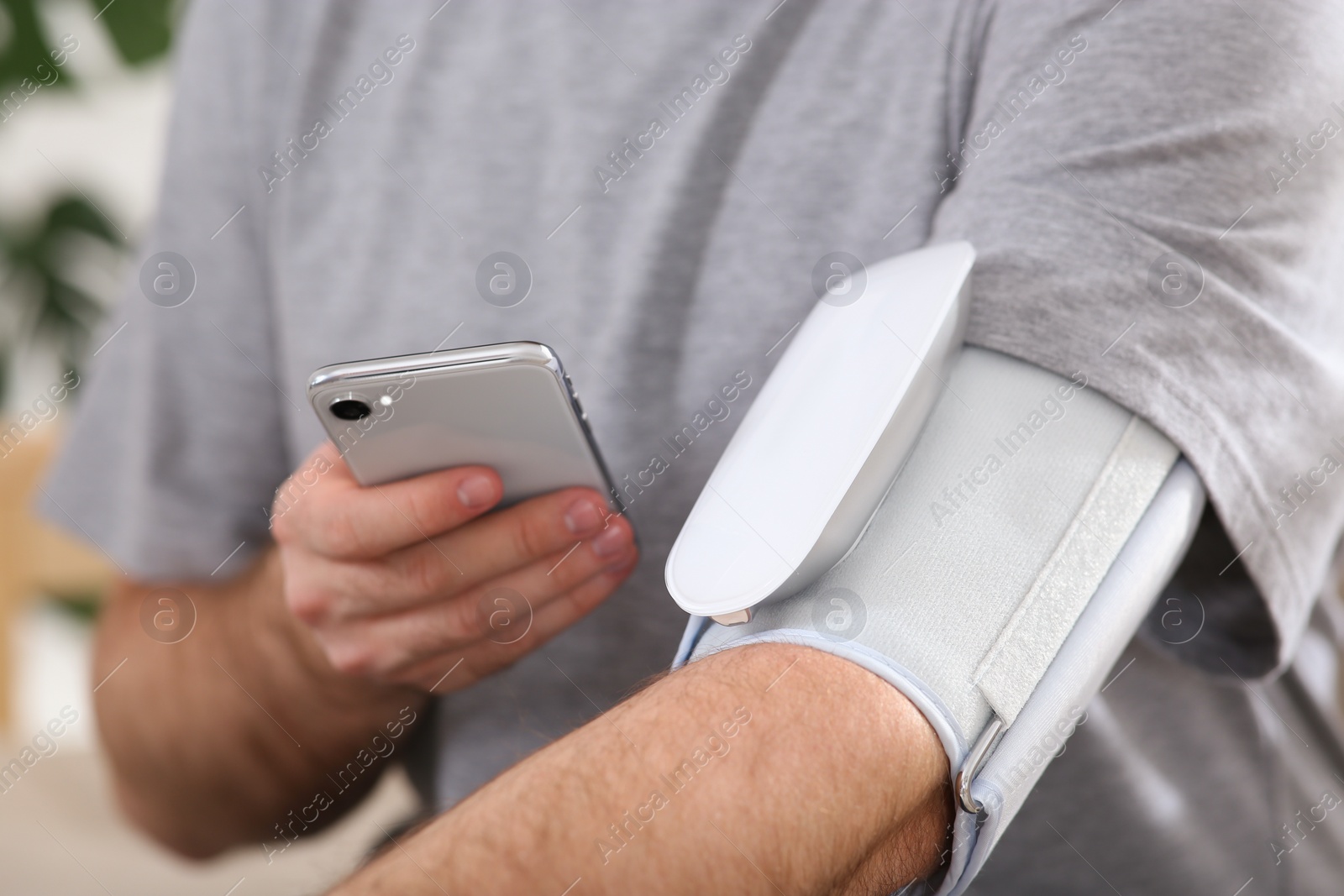 Photo of Man checking blood pressure with modern monitor and smartphone indoors, closeup