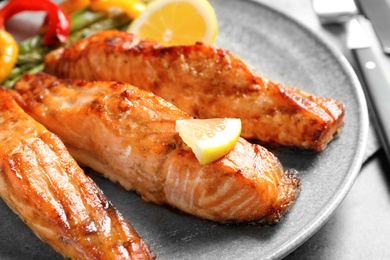 Tasty cooked salmon with lemon on plate, closeup