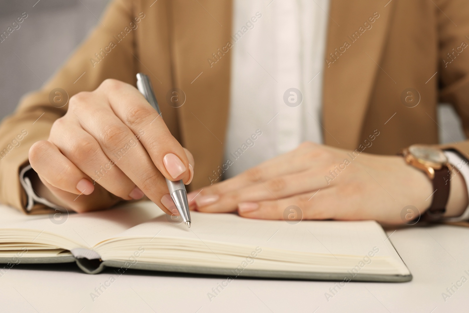 Photo of Woman writing in notebook at white table, closeup