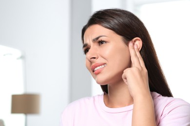 Photo of Young woman suffering from ear pain indoors, space for text