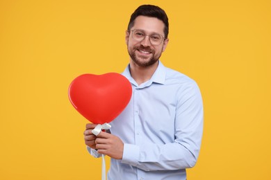 Photo of Man holding red heart shaped balloon on yellow background