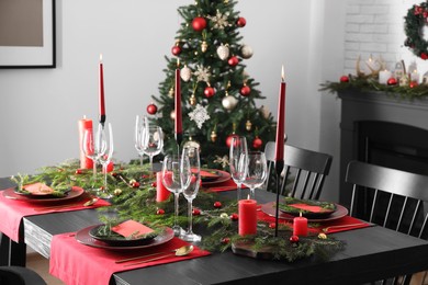 Photo of Elegant Christmas table setting with dishware and burning candles in festively decorated room