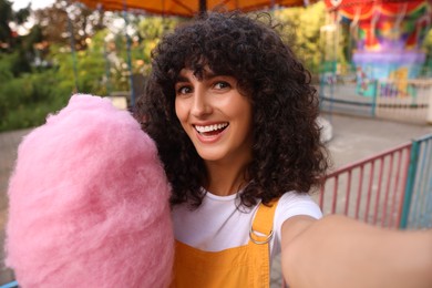 Photo of Smiling woman with cotton candy taking selfie at funfair
