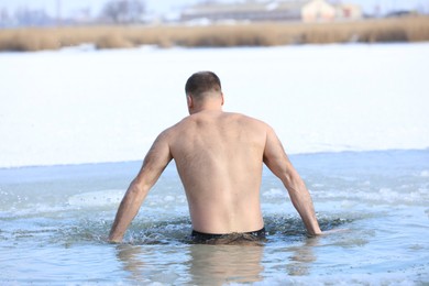 Photo of MYKOLAIV, UKRAINE - JANUARY 19, 2021: Man immersing in icy water on winter day, back view. Traditional Baptism ritual