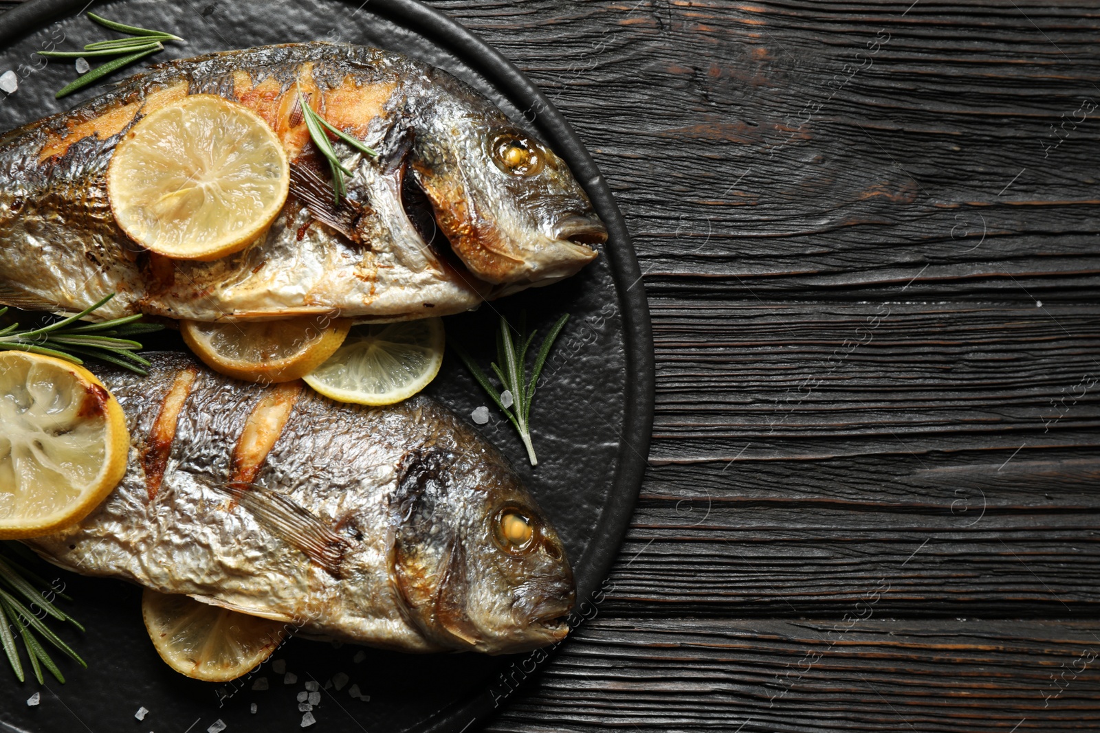 Photo of Delicious roasted fish with lemon on black wooden table, top view. Space for text
