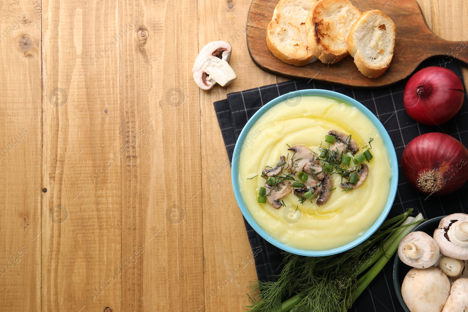 Photo of Bowl of tasty cream soup with mushrooms, green onions and dill on wooden table, flat lay. Space for text