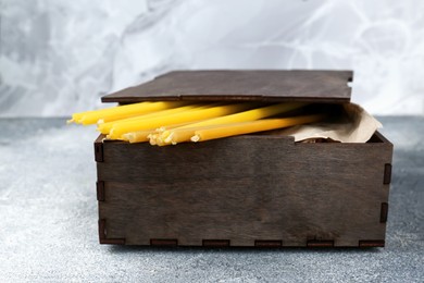 Photo of Wooden box with church candles on grey textured table, closeup