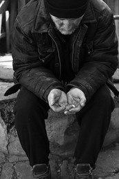 Photo of Poor homeless senior man holding coins outdoors. Black and white effect