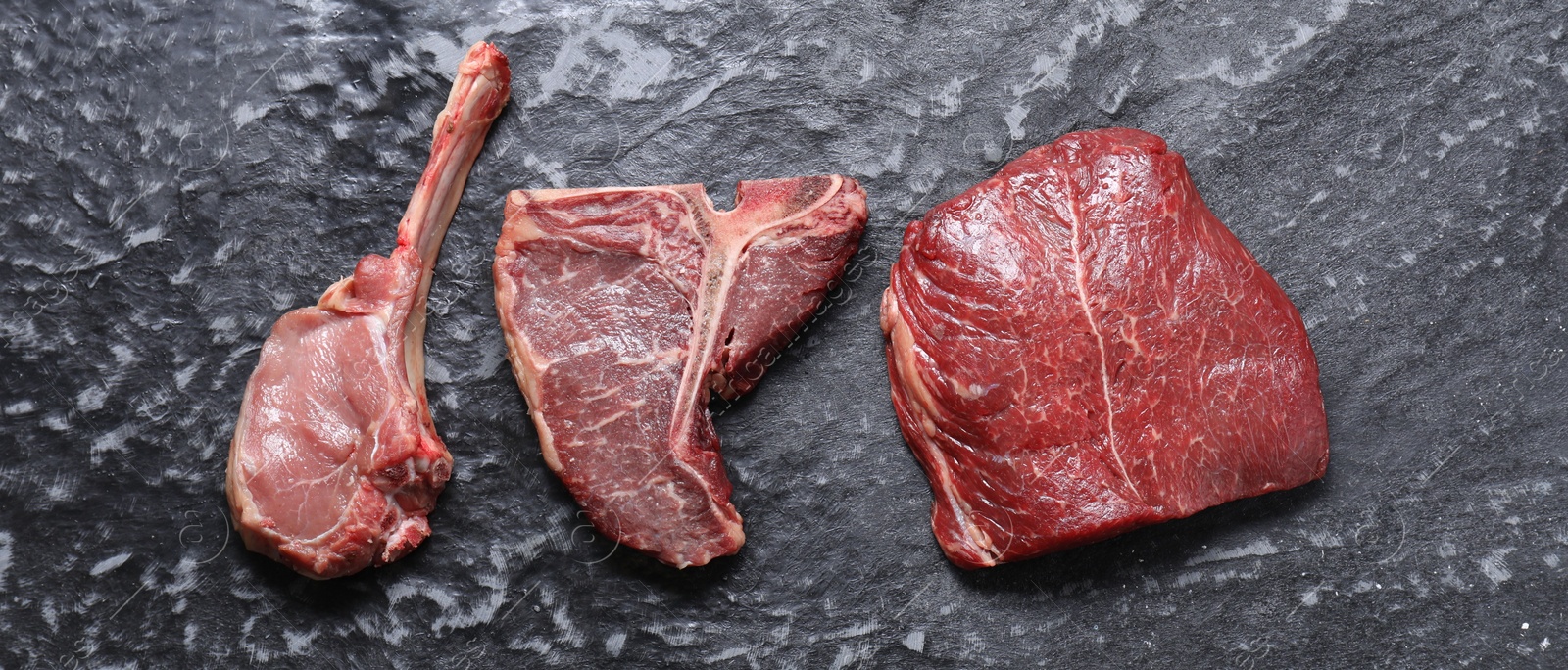 Photo of Fresh raw beef cuts on grey textured table, flat lay