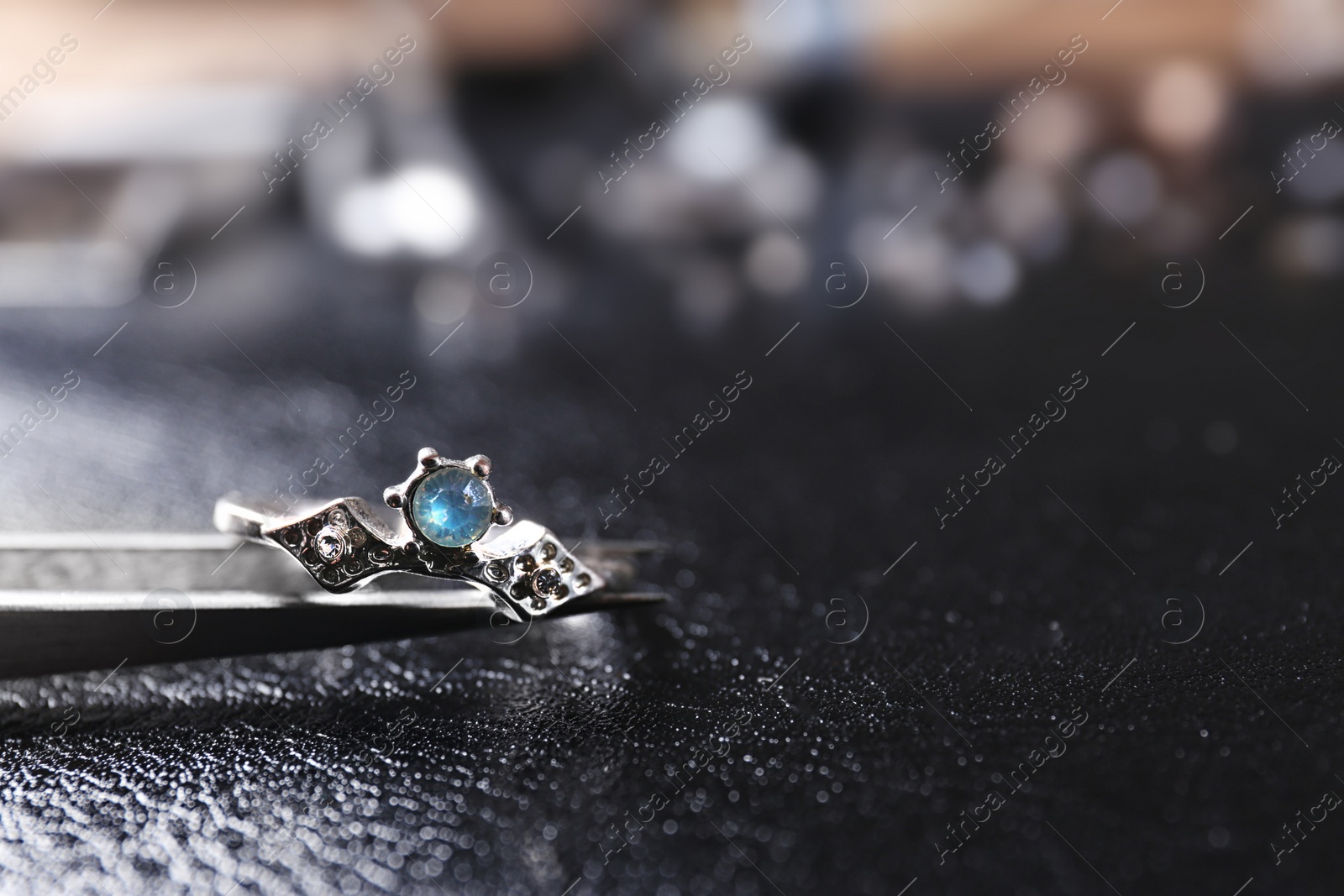 Photo of Elegant ring on black leather surface, closeup view. Precious jewellery