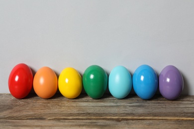 Photo of Easter eggs on wooden table against light grey background, space for text
