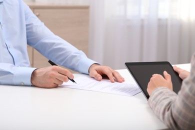 Photo of Businesspeople signing contract at white table in office, closeup of hands