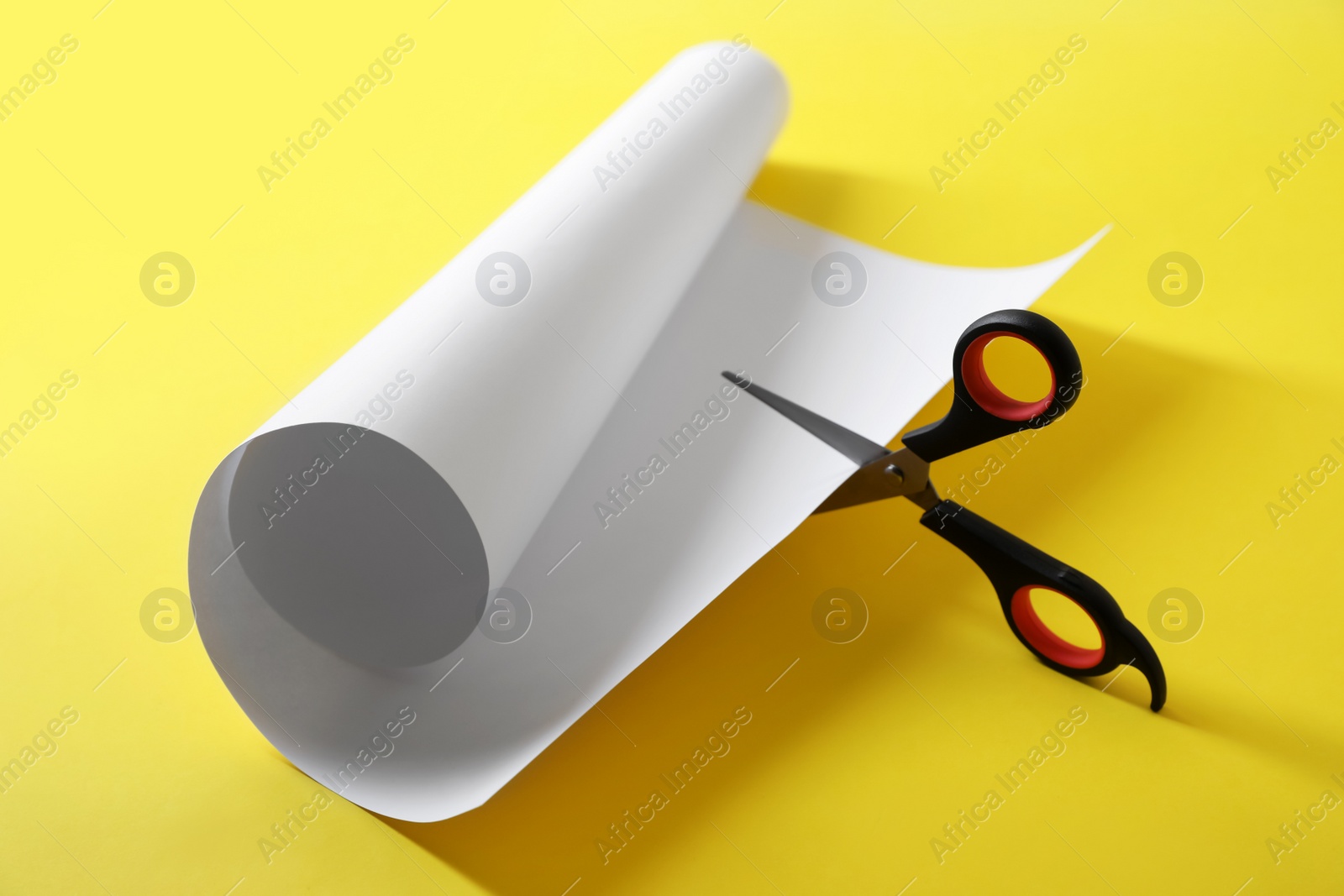 Photo of Scissors cutting white paper on yellow background