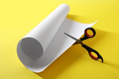 Photo of Scissors cutting white paper on yellow background