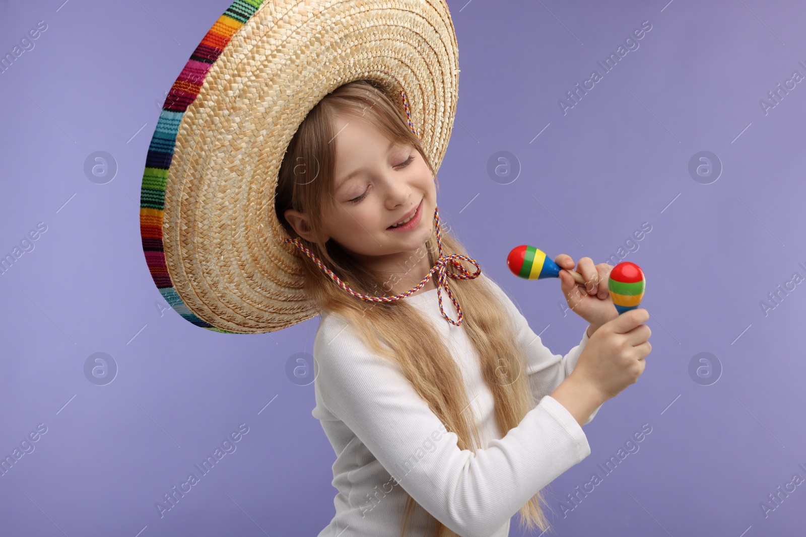 Photo of Cute girl in Mexican sombrero hat dancing with maracas on purple background