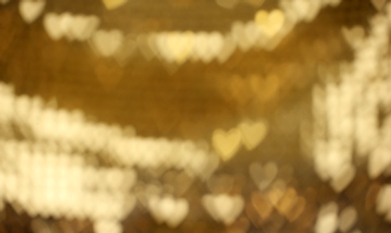 Blurred view of beautiful heart shaped lights on gold background