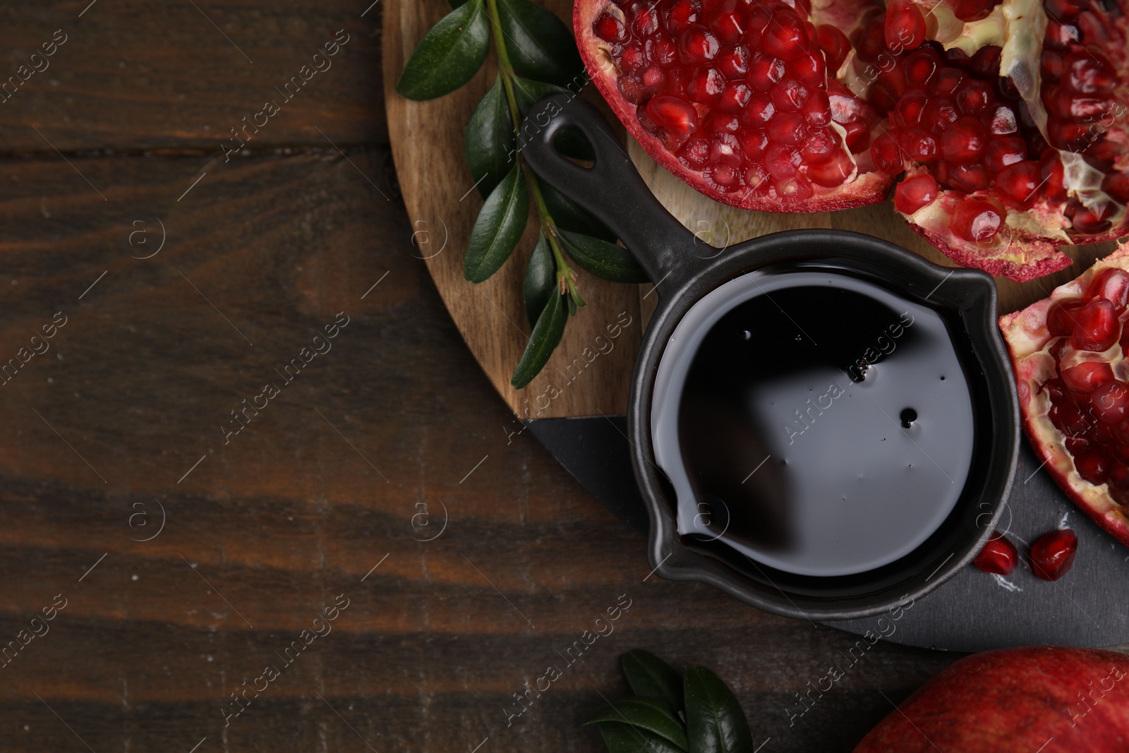 Photo of Tasty pomegranate sauce, fruits and branches on wooden table, top view. Space for text