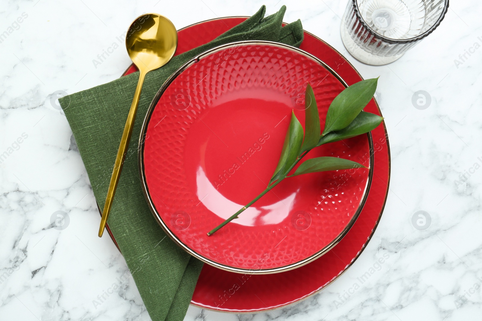 Photo of Stylish ceramic plates, spoon, glass and floral decor on white marble table, top view