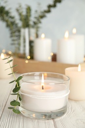 Burning aromatic candle and eucalyptus branch on table. Space for text