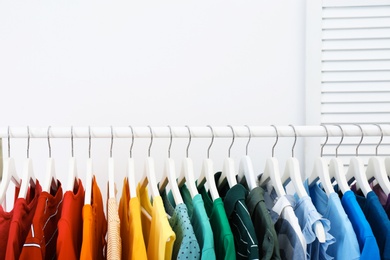 Photo of Rack with bright clothes in room. Rainbow colors