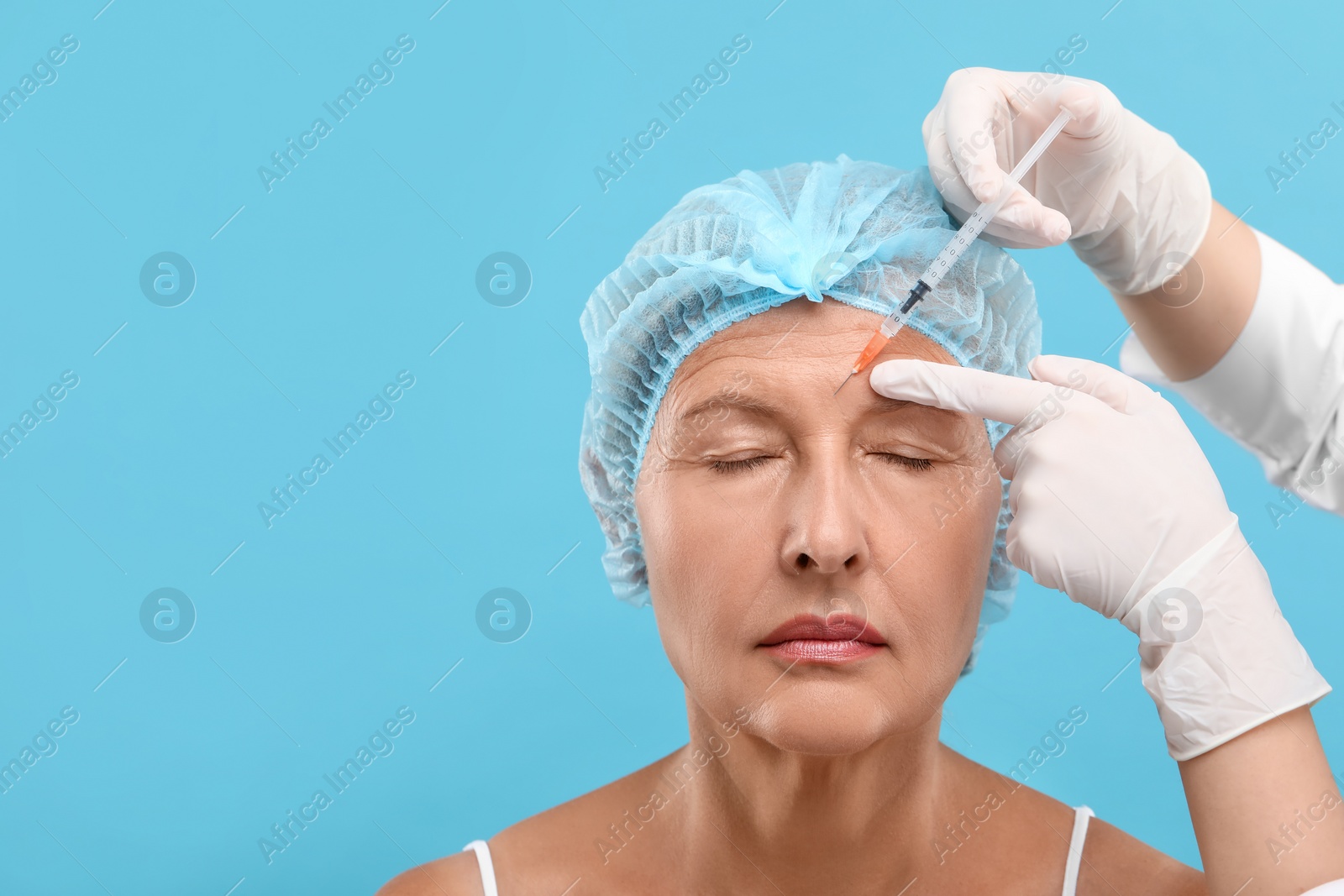 Photo of Doctor giving facial injection to senior woman on light blue background, space for text. Cosmetic surgery