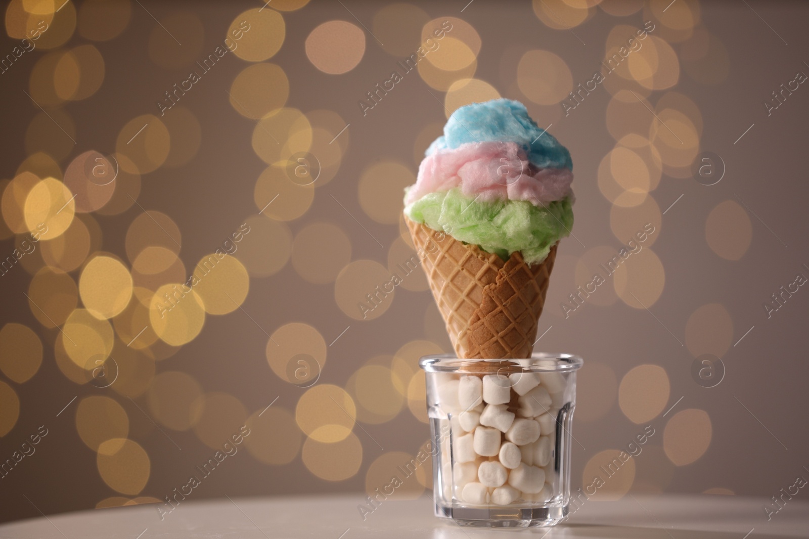 Photo of Sweet cotton candy in waffle cone on table against blurred lights, closeup. Space for text