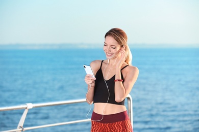 Photo of Young woman choosing music for fitness exercises on pier in morning