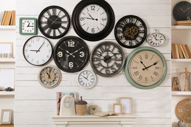 Collection of clocks hanging on white wall above mantel indoors