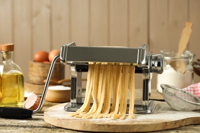 Pasta maker with raw dough on wooden table